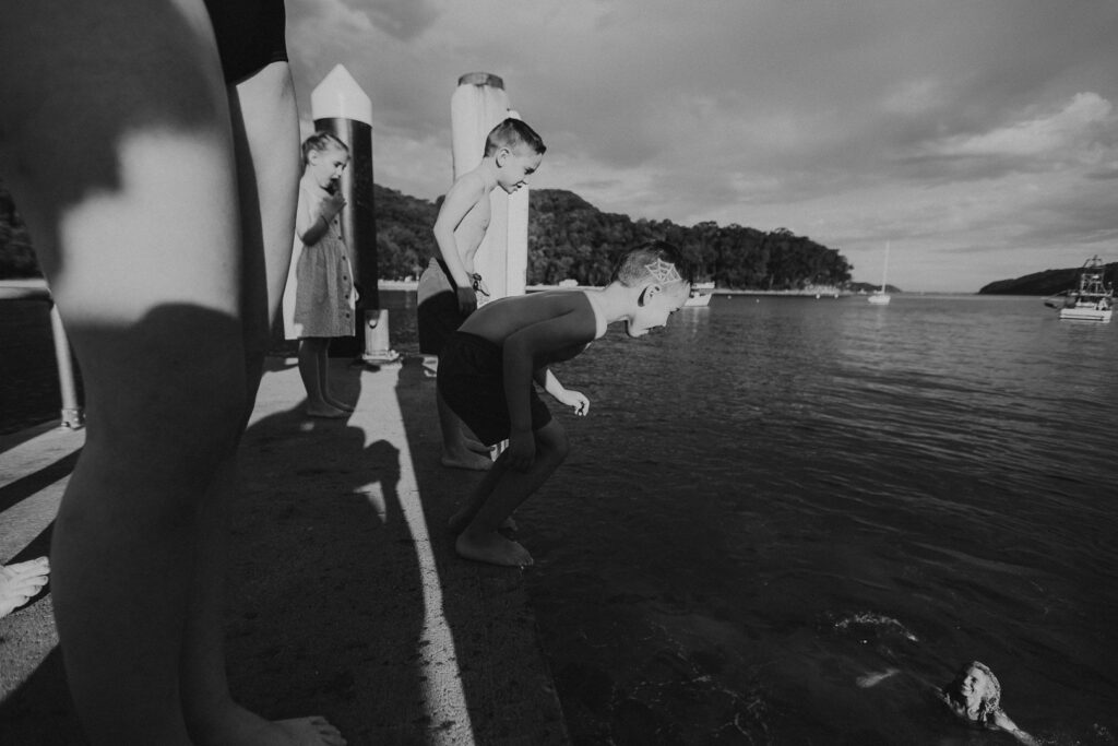 A young boy about to jump off a boat wharf into the ocean below. Fun, natural and real family photography sessions