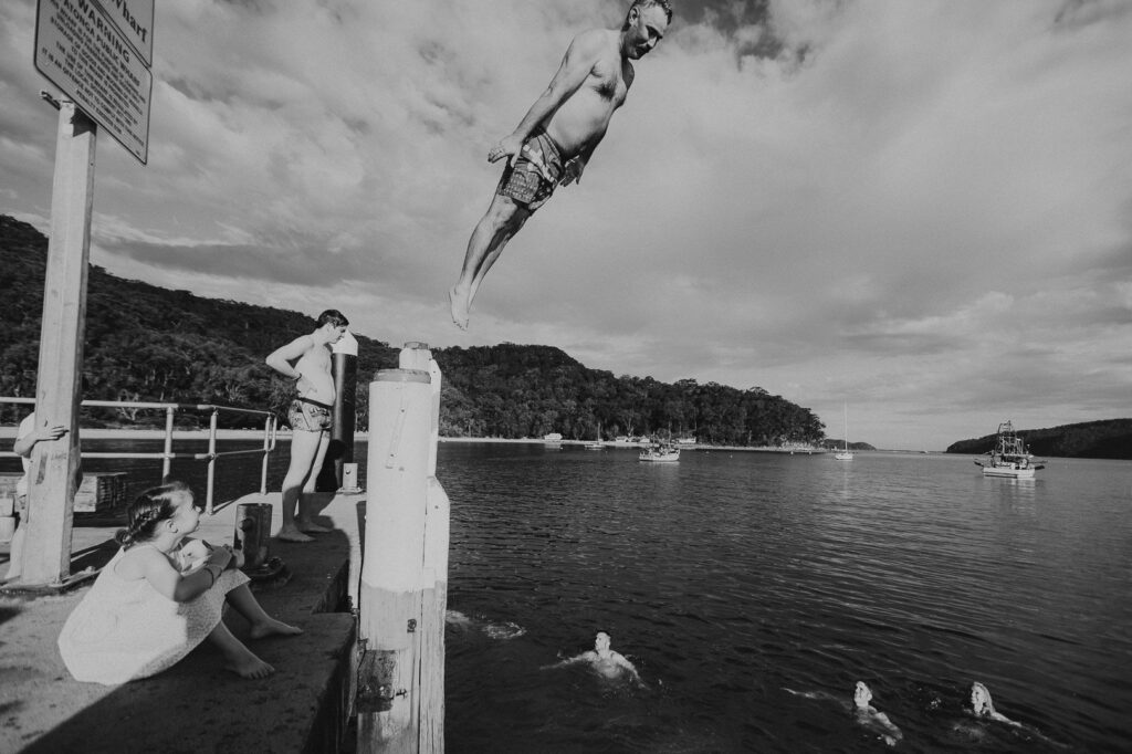 Man jumping off the ferry wharf in a comedic penguin-like pose during a family photography session