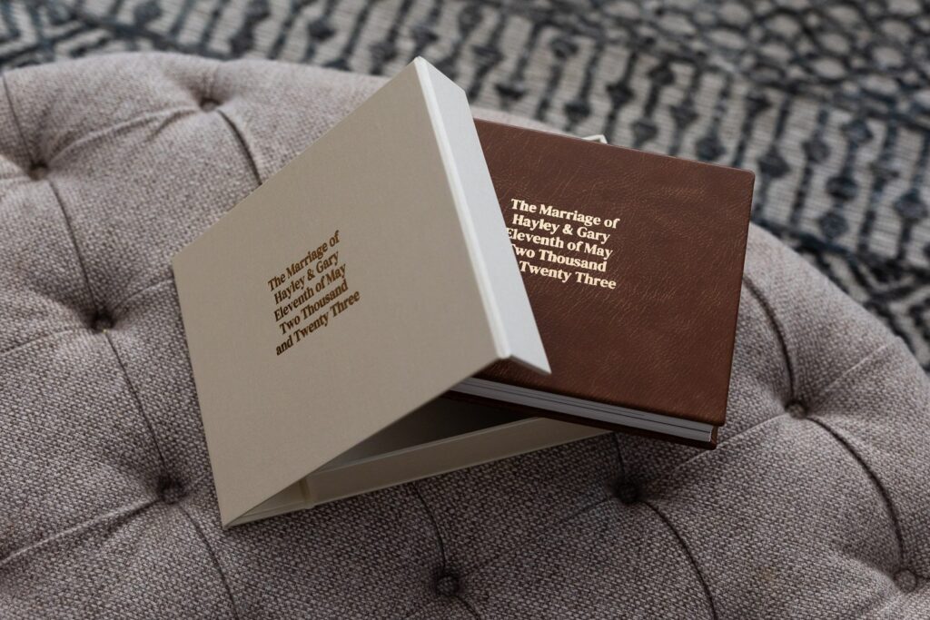 A genuine leather Fine Art Wedding Album with a Designer Album Case lying on top of a cloth coffee table. The albums are embossed with gold foiled writing.