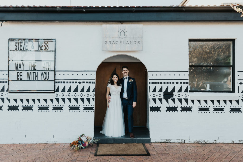 Couple standing in the doorway of Gracelands Forresters Beach, a Central Coast Wedding Venue. The sign reads May the fourth be with you