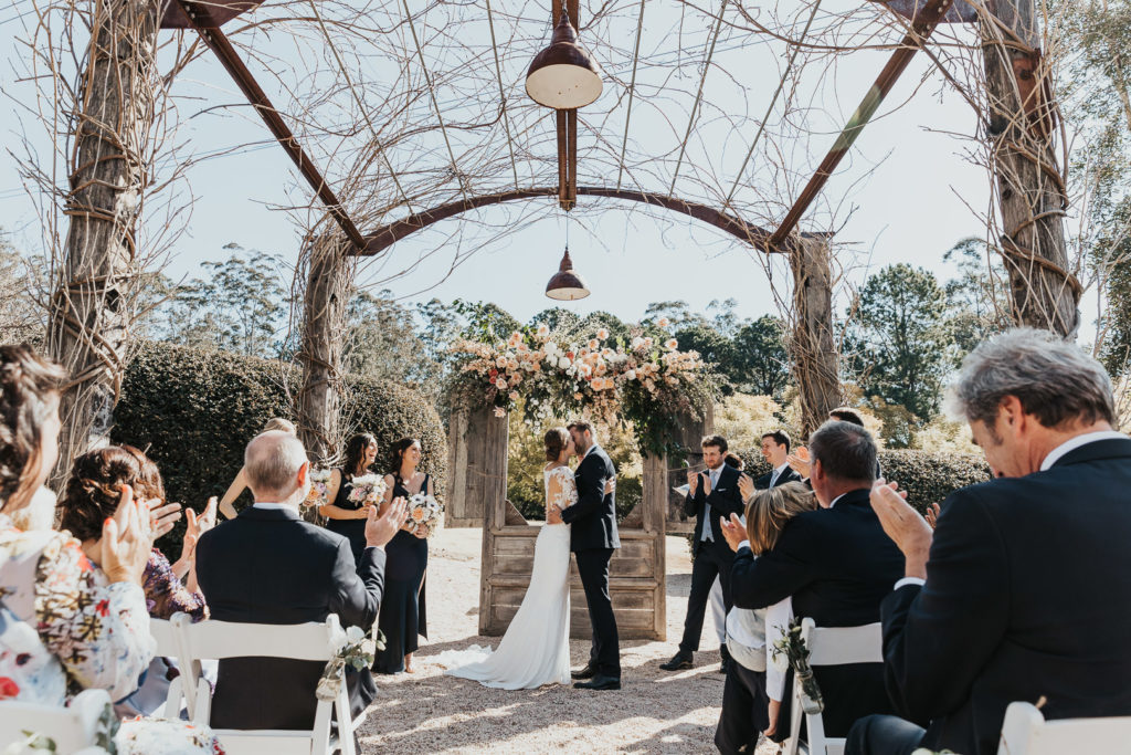 A beautiul large pagola arbour at Yarramalong Fernbank Farm. The wedding couple kiss at the front of the guests