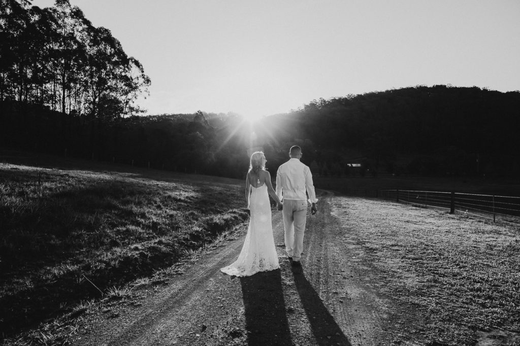 Black and white photo of a couple walking down a dirt track towards the setting sun holding hands in the Hunter Valley