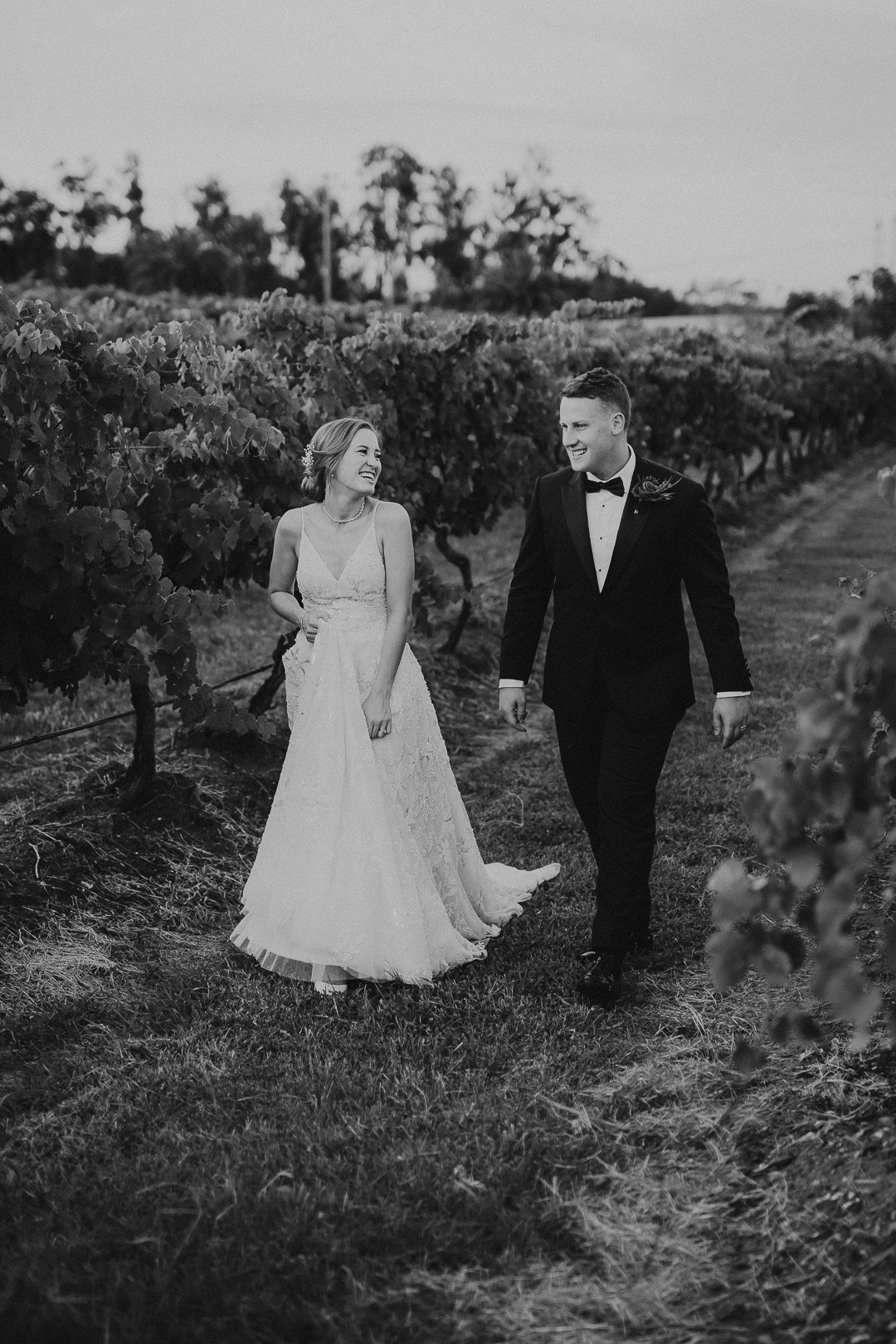 A couple walking through the vines in the vineyard at Bimbadgen Palmers Lane wedding venue in the hunter valley. it is a black and white image which looks classy and elegant but still fun!