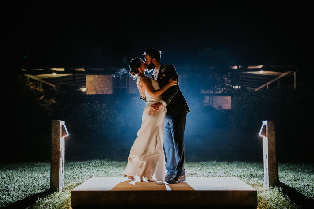 Night photo of a couple kissing. It is a Wedding at Glenworth Valley on the NSW Central Coast. They are backlit and there is mist. It looks cold but romantic