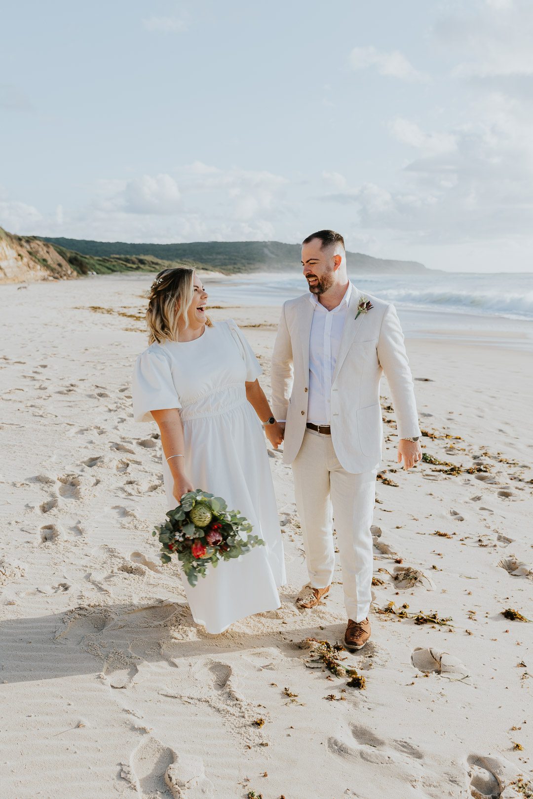 Sunrise Beach Elopement Photography Sydney. A happy and relaxed looking couple wander down the beach laughing on their Elopement Wedding. The image is colouful, fresh and fun.