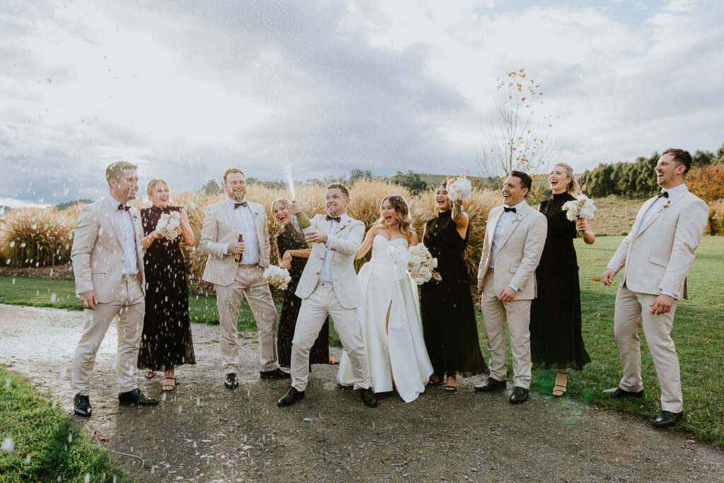 A Wedding Party sprays Champagne around in front of Pampas Grasses at Bendooley Estate near Bowral in the NSW Southern Highlands. Fun and stylish Wedding Photography makes for a light-hearted image at sunset