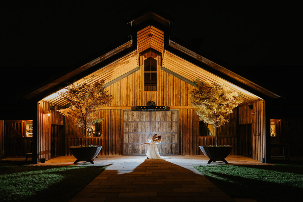 Epic night wedding photo at Bendooley Estate Stables showing the bride and groom having a kiss and drop dance pose whilst being backlit with flash to make them stand out against the background. South Coast Wedding Photographer Underatreehouse