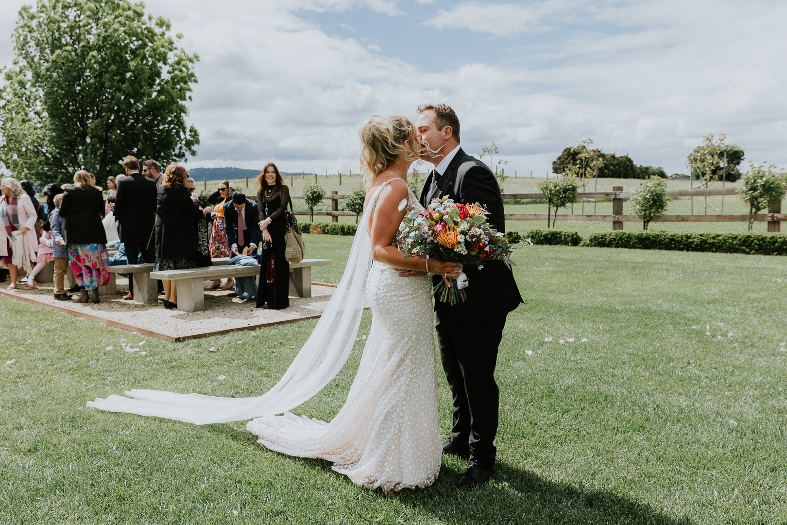 A couple kiss at the end of the aisle at the end of their wedding ceremony at BoxGrove Bathurst. Colourful and fun photography